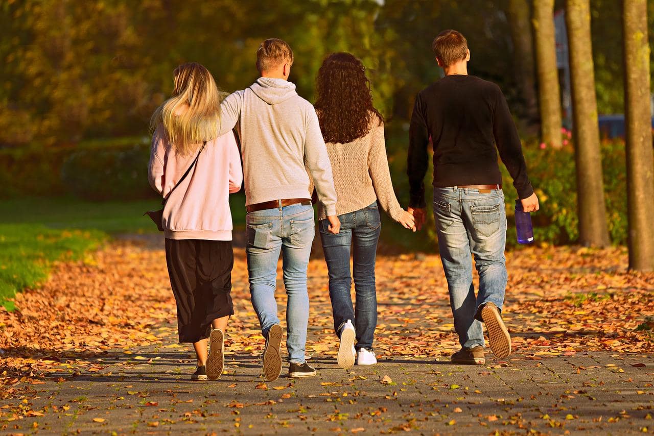 Four friends walking together along a leaf-covered path