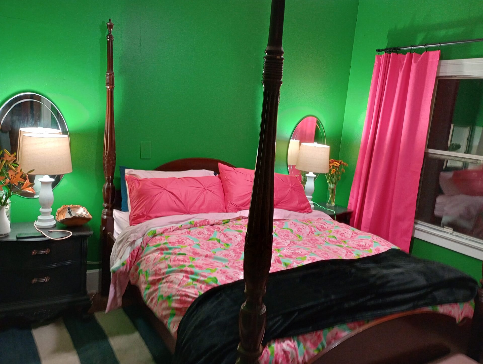 Completed bedroom transformation with a four-poster bed, bedside tables, lamps, mirrors, floral bedding and bright pink curtains.