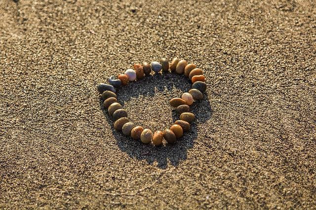 warmly lit photograph of wet beach sand with small pebbles arranged in the shape of a heart