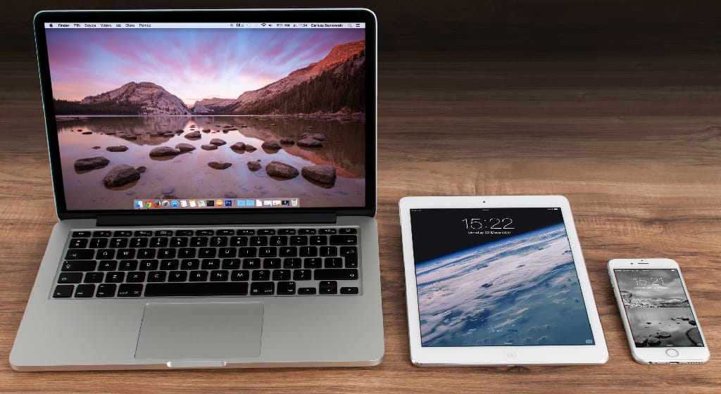 photograph of a wooden table top on it is an apple laptop computer, and iPad, and an iPhone