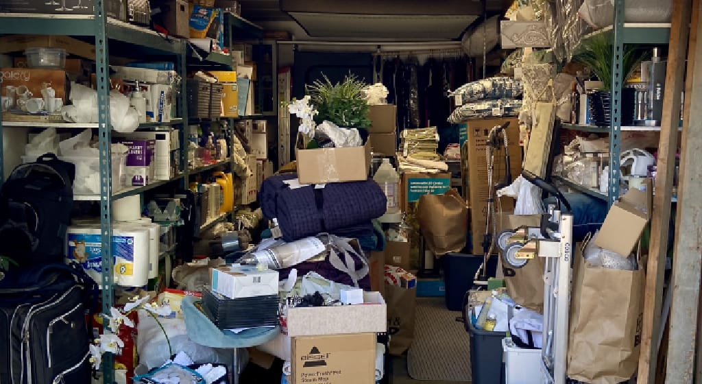 photo image of an open single car garage full of boxes, cleaning supplies, food, tools, luggage, clothes, etc.